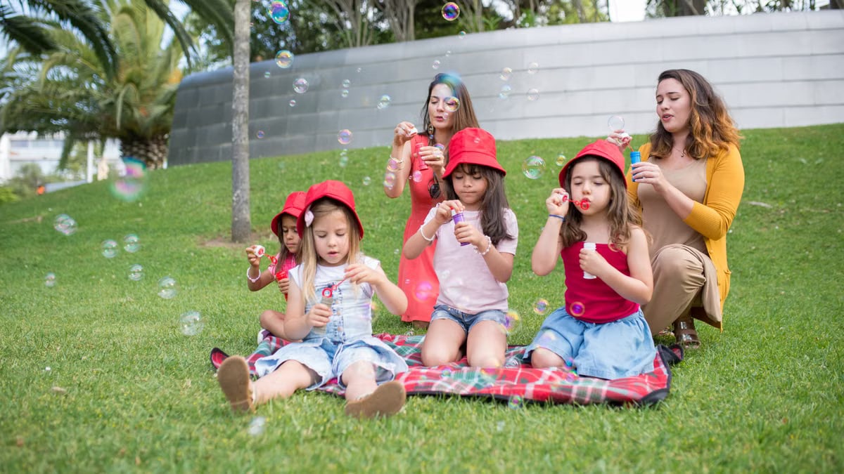 Group of children and adults blowing bubbles in a sunny park setting.